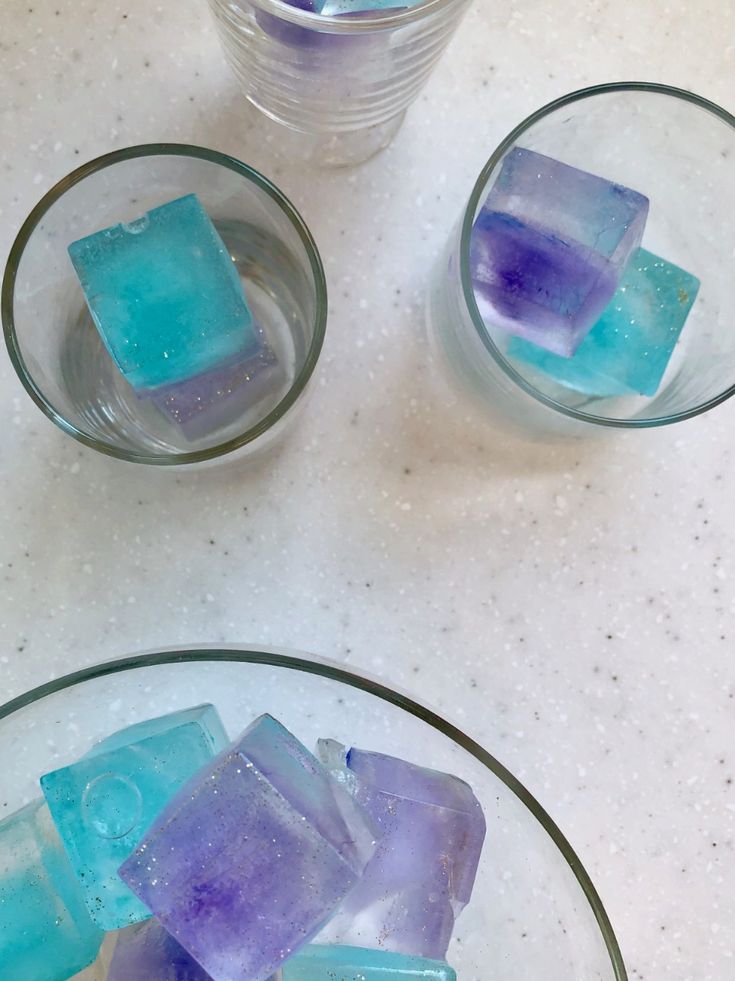 three glass bowls filled with ice cubes on top of a white counter next to a cup