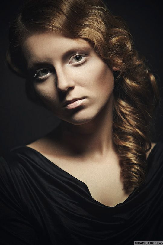 a woman with long red hair and blue eyes is posing for a photo in the dark