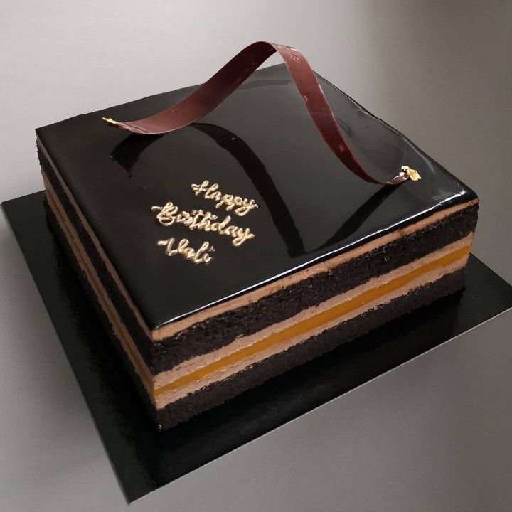 a black and gold birthday cake with a brown ribbon on it's top is sitting on a table