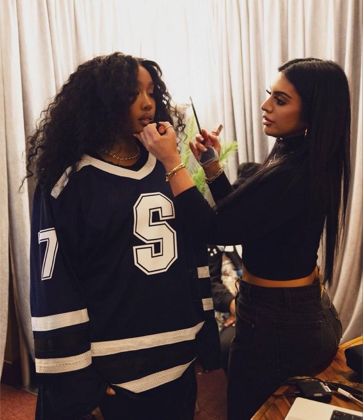 two women standing next to each other in front of a window brushing their teeth and looking into the mirror