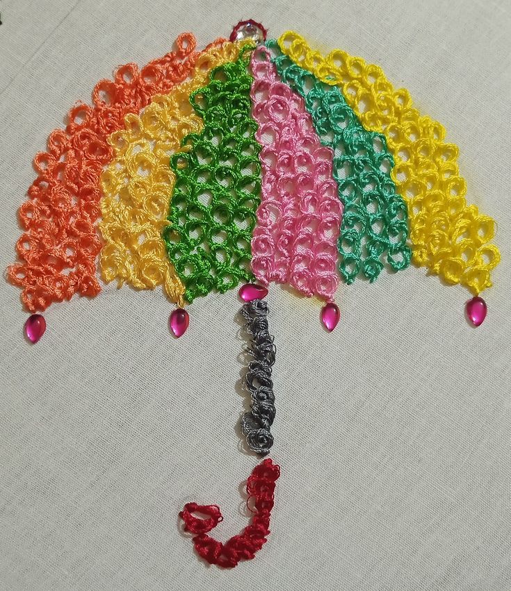 an umbrella made out of beads on a white cloth with the letter j in red, yellow, green, blue and pink