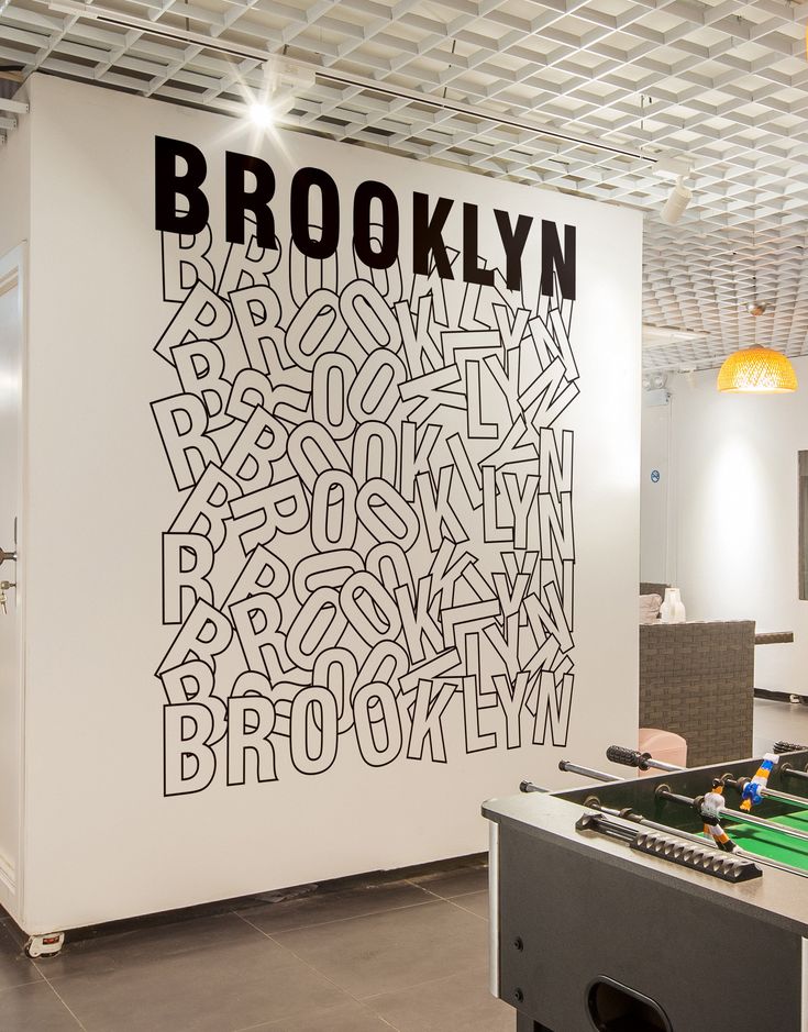 a room with a foosball table in the center and a large brooklyn sign on the wall