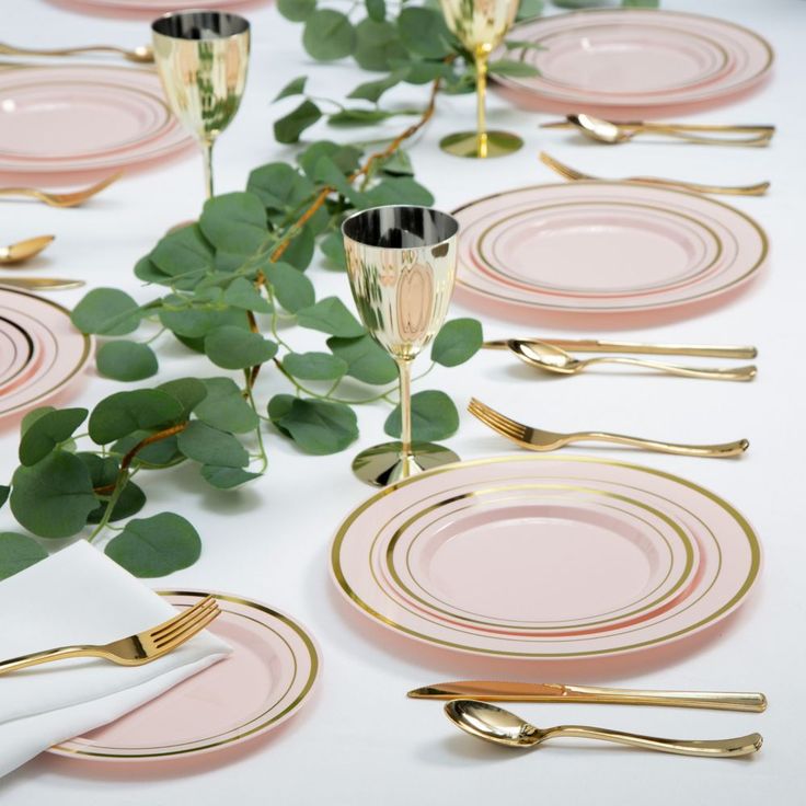 the table is set with pink and gold plates, silverware, and greenery