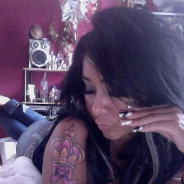 a woman with long black hair and tattoos on her arm holding a cell phone to her ear