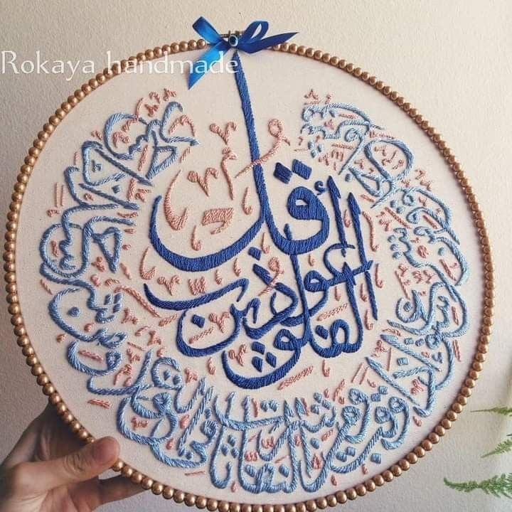 a person holding up a embroidery work with arabic writing on it