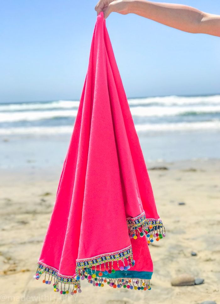 a pink towel hanging from the side of a persons hand on a beach with waves in the background