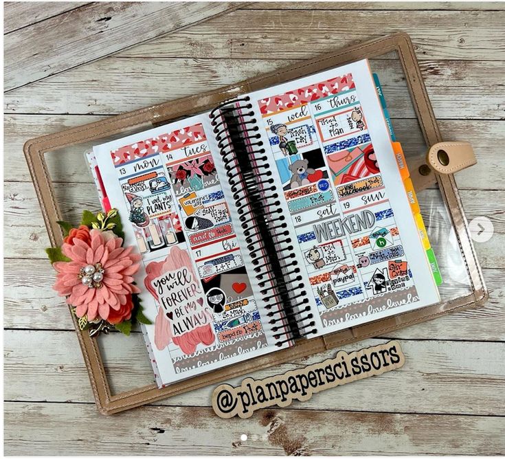 an open notebook with stickers on it and a pink flower in the middle, sitting on top of a wooden table