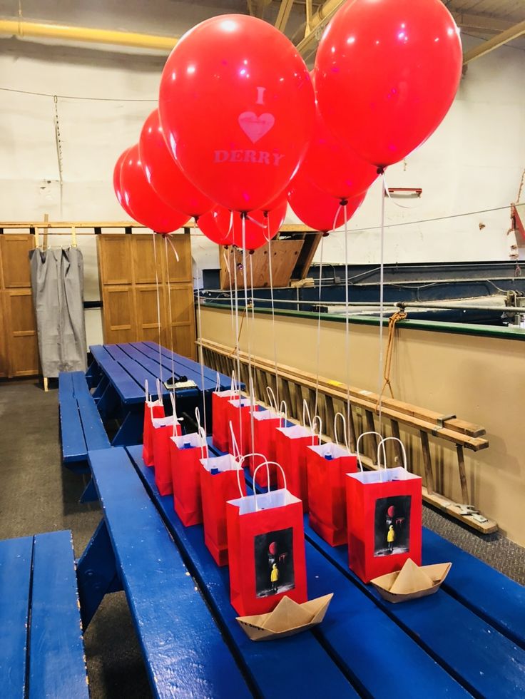 some red balloons are hanging from bags on a blue table in a room with wooden benches