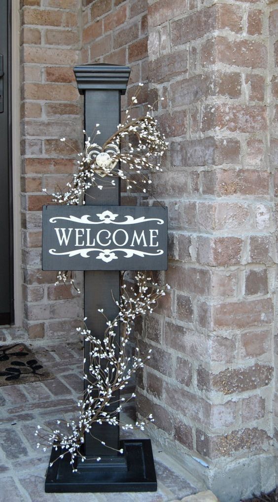 a welcome sign on the side of a brick building next to a lamp post with flowers growing out of it