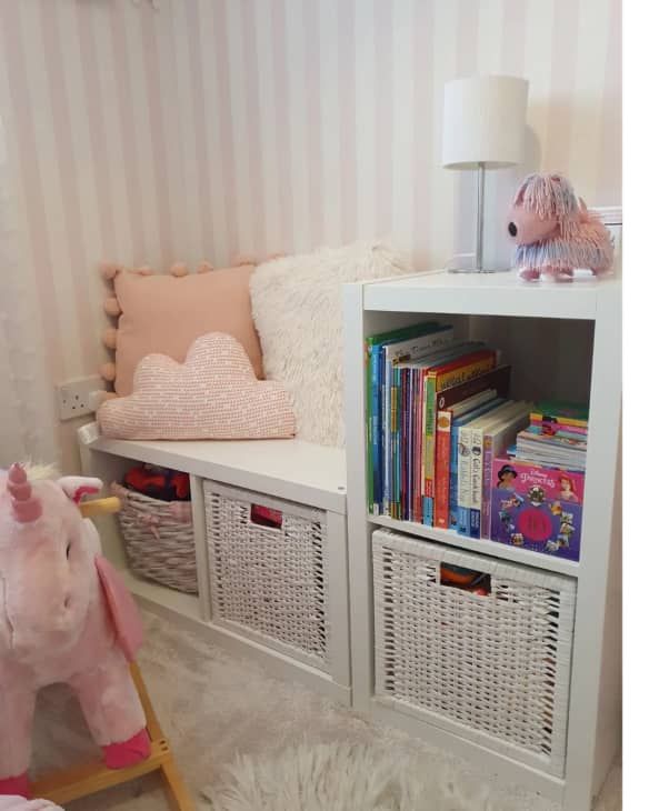 a white book shelf filled with books next to a pink stuffed animal and other toys