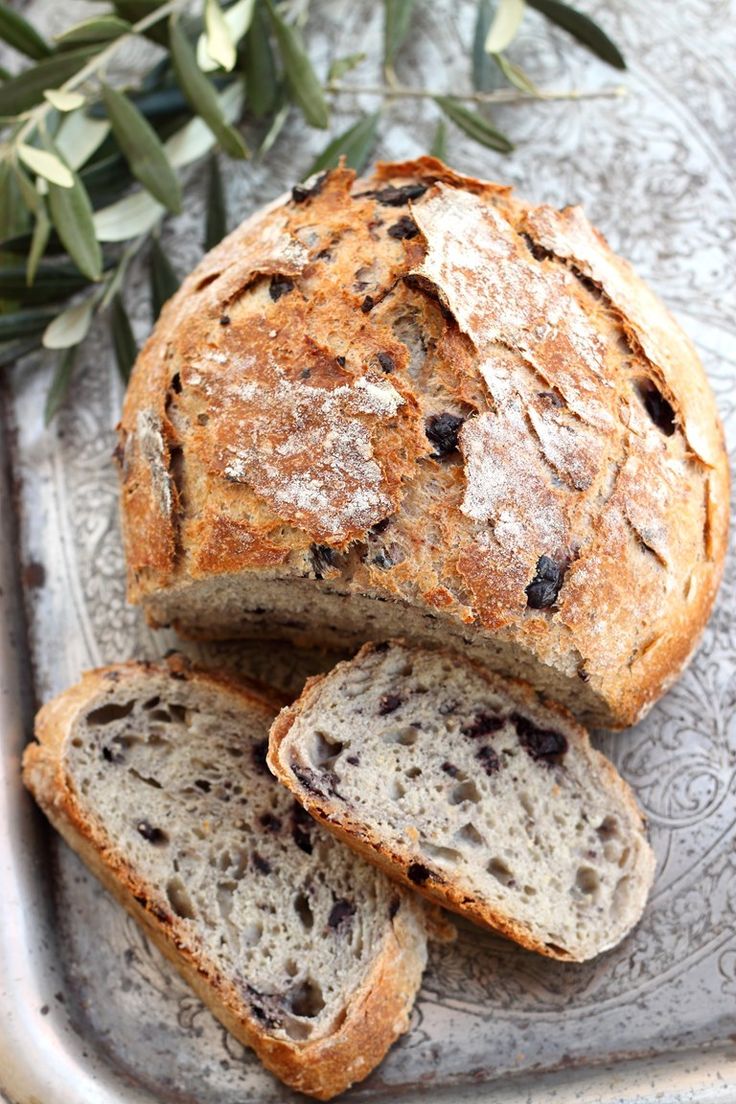 bread with raisins is sitting on a silver platter next to an olive branch