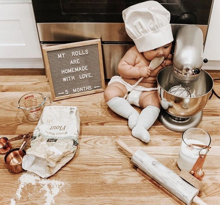 a baby sitting on the floor next to a mixer and other kitchen items, including flour