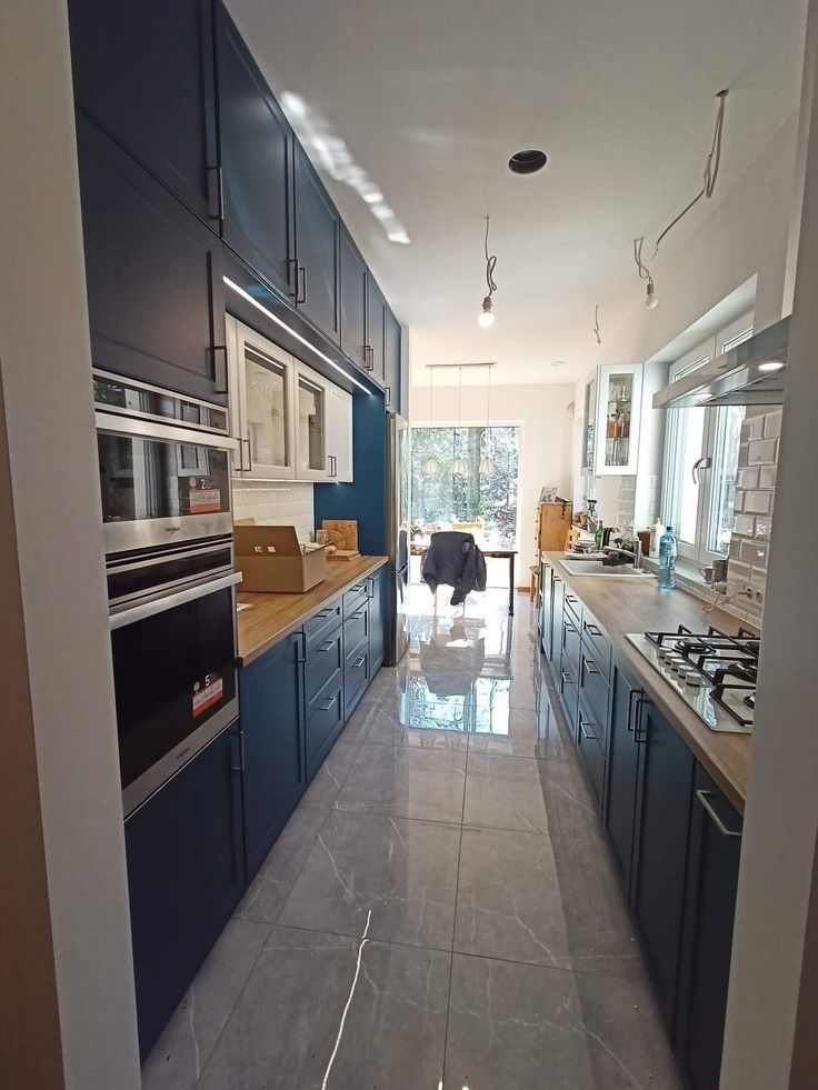 a long kitchen with blue cabinets and white counter tops is seen through an open door