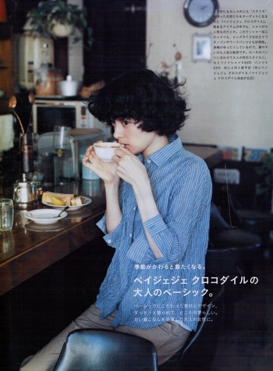 a woman sitting at a table drinking from a cup