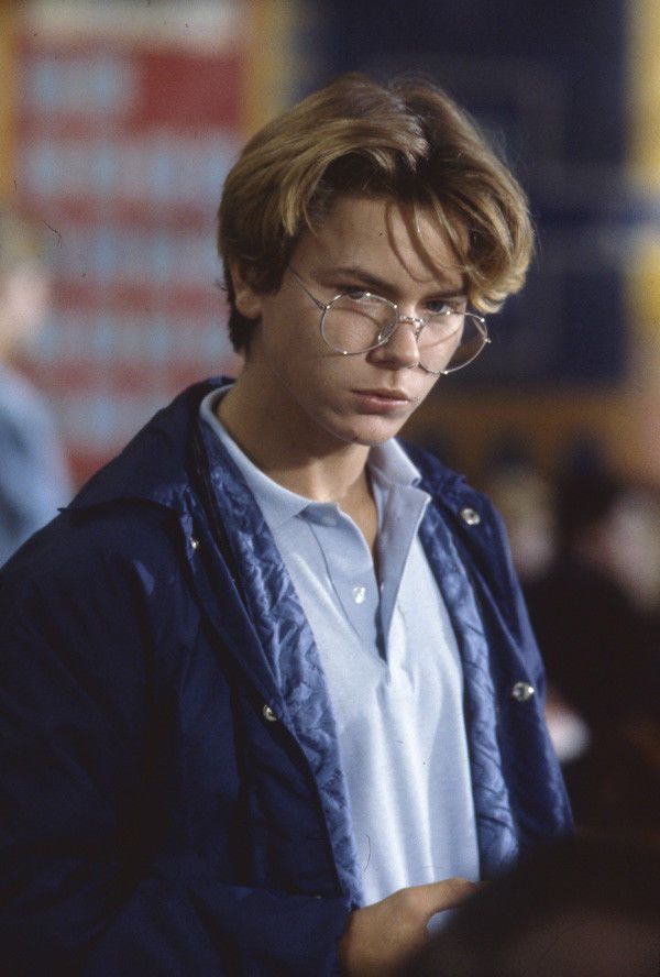 a young man wearing glasses looking down at his cell phone while standing in front of a crowd