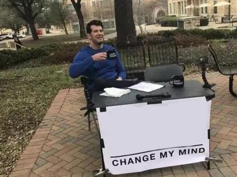 a man sitting at a table with a sign that says change my mind