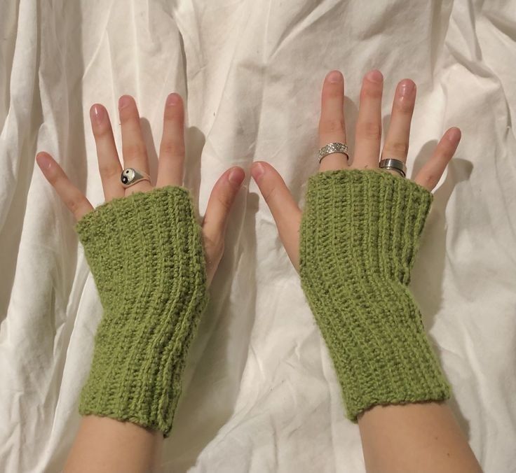 two hands wearing green knitted gloves on top of a white sheet