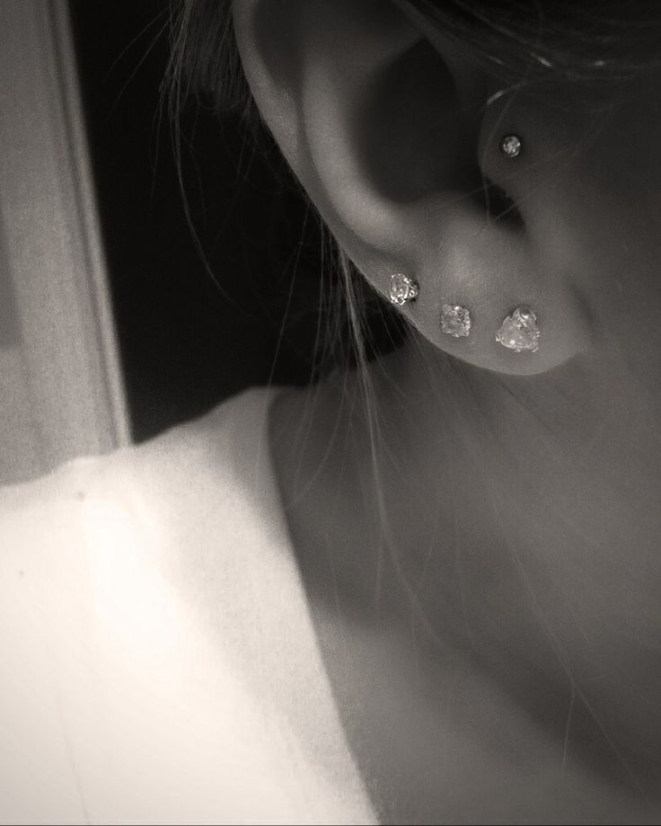 black and white photograph of a woman's ear with three diamond studs on it