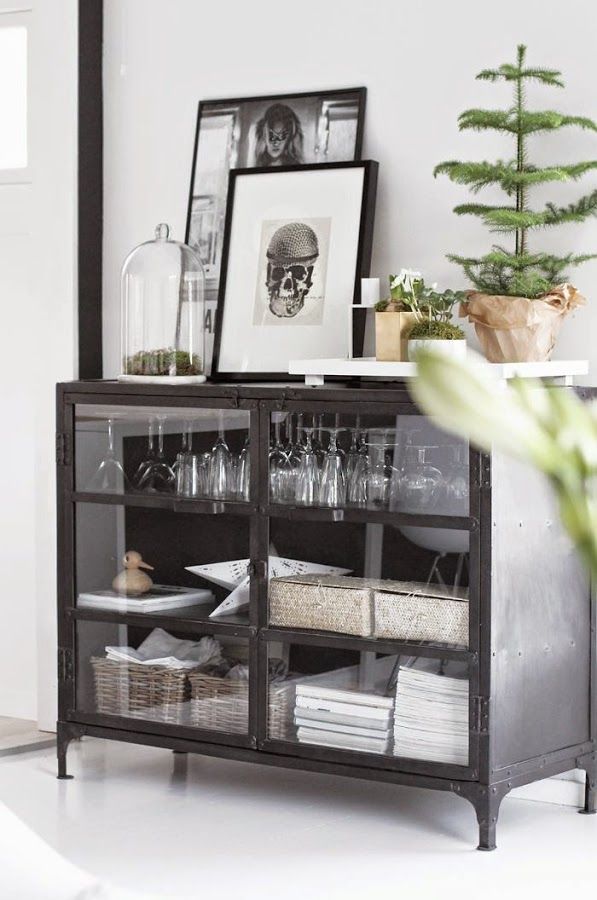 a black cabinet filled with wine glasses next to a potted plant and framed pictures