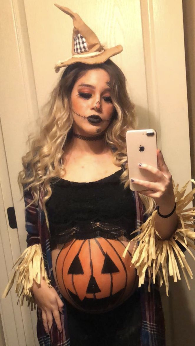 a pregnant woman dressed up as a witch holding a cell phone in her right hand