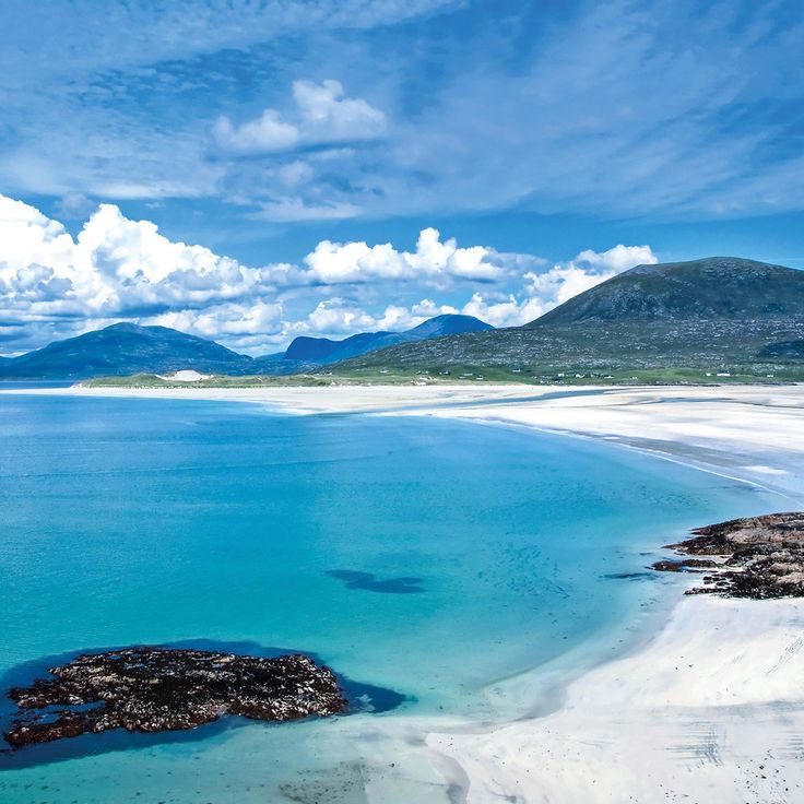 an aerial view of the water and sand at low tide beach, with mountains in the distance