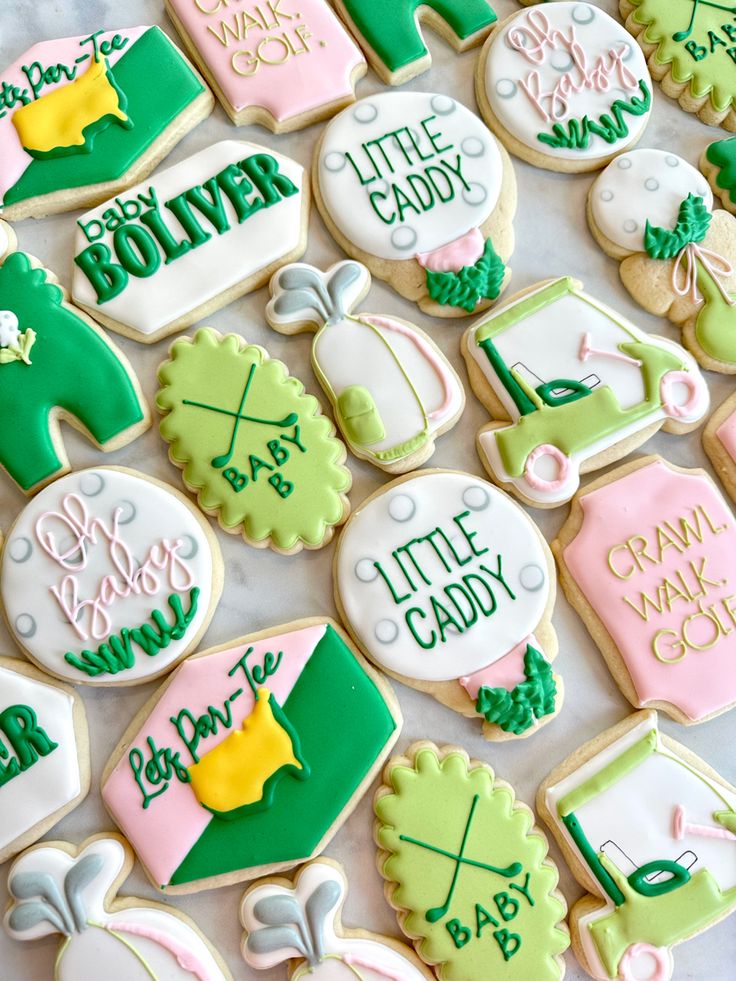 baby shower cookies decorated with green, pink and white icing are on a table