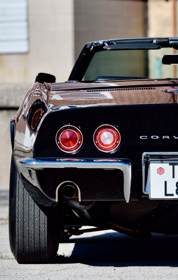 the back end of a black corvette car parked in front of a building with its license plate