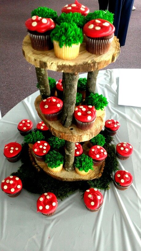 three tiered cupcake stand with mushrooms and trees on the top, surrounded by red muffins