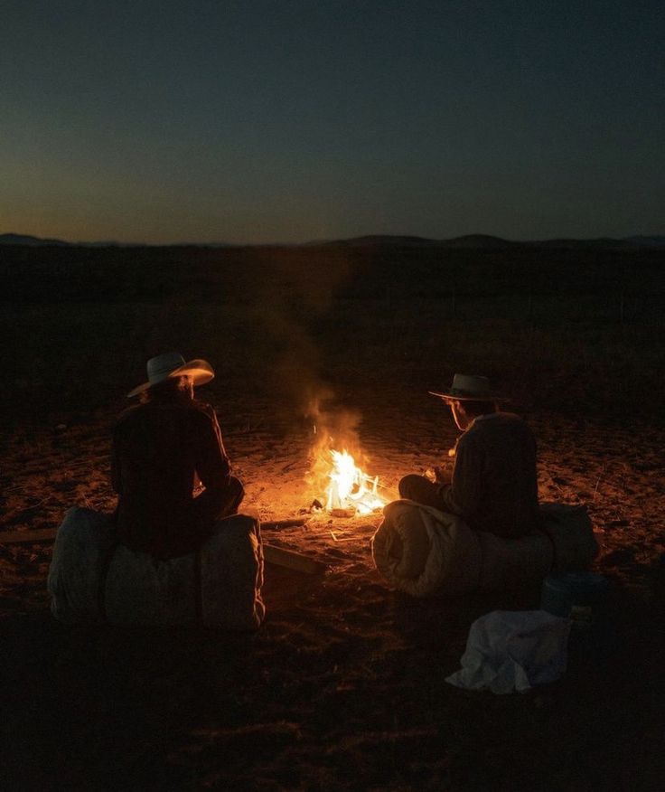 two people sitting around a campfire in the middle of nowhere at night with their backs to each other