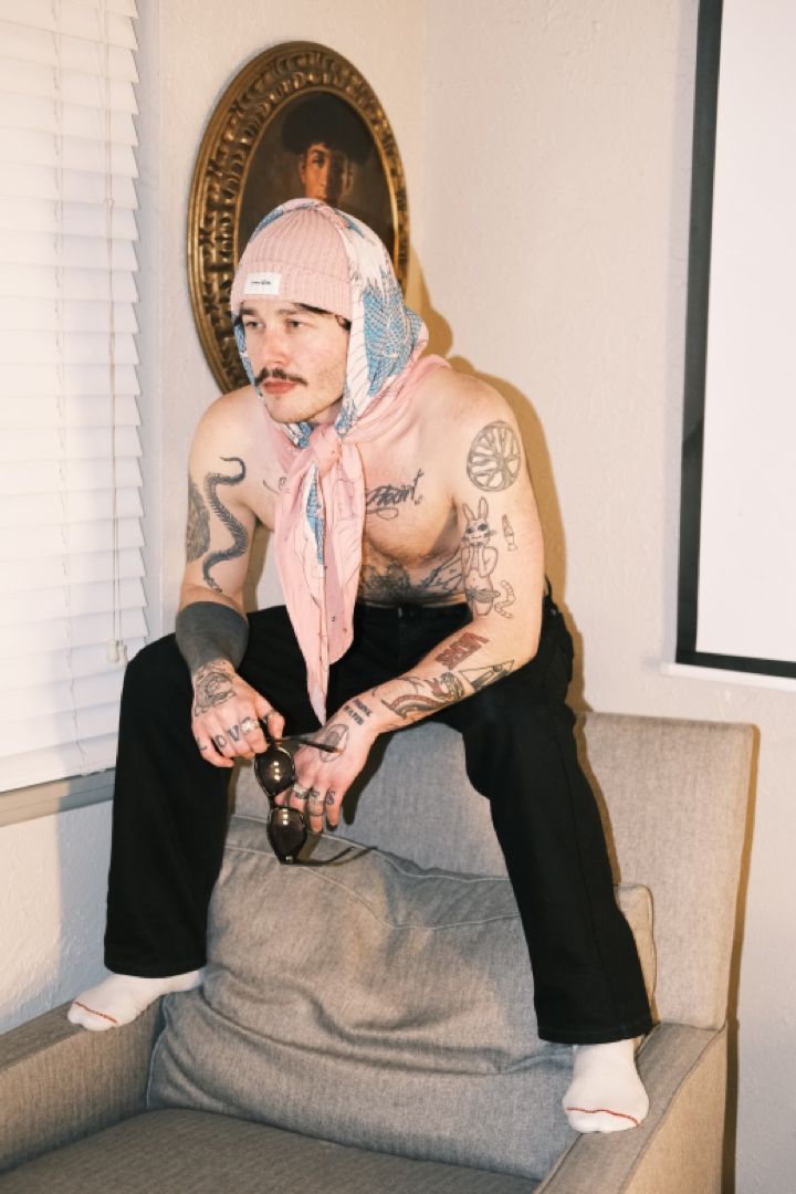 Man wearing dragon print scarf over beanie sitting on top of chair. Men In Head Scarfs, Silk Scarf Outfit Men, Bandana Outfit Men, White Sunglasses Outfit, Scarf Outfit Men, Summer Fits Men, Mens Scarf Fashion, Silk Scarf Outfit, Cargo Pants Outfit Men