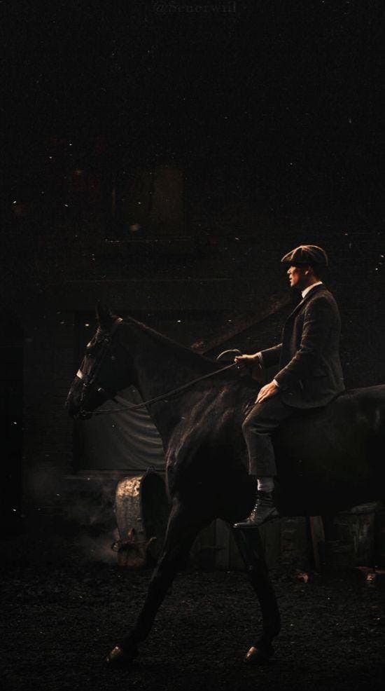 a man riding on the back of a brown horse in an enclosed area at night