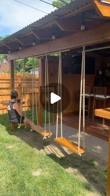 a woman sitting on a swing set in the grass next to a wooden fence and building