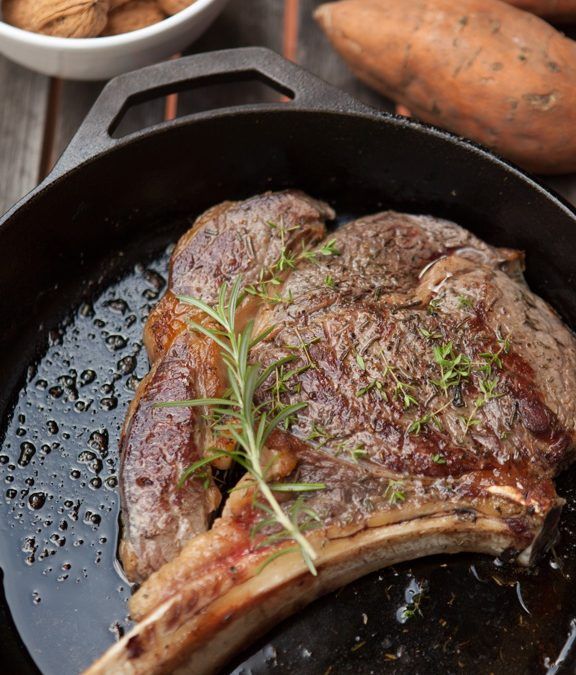 a steak in a cast iron skillet next to sweet potatoes