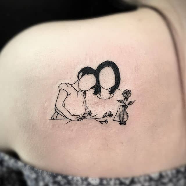 a woman's back shoulder with a tattoo of two people holding each other in front of her