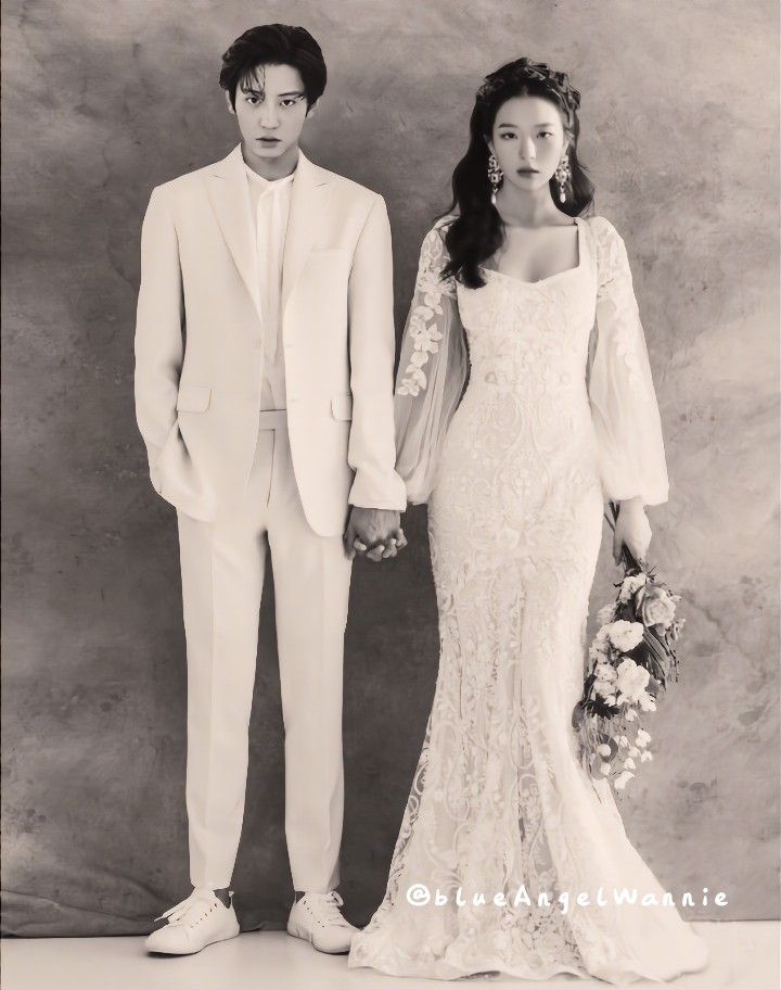 a man and woman standing next to each other in front of a gray wall holding hands