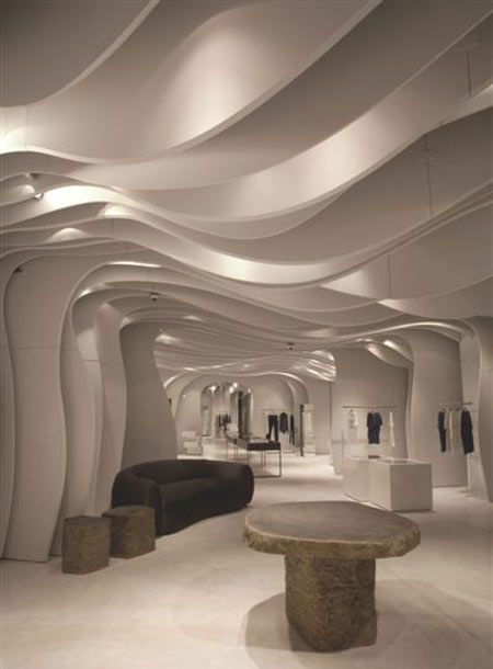 the interior of a modern fashion store with white walls and curved ceilings, stone benches and stools