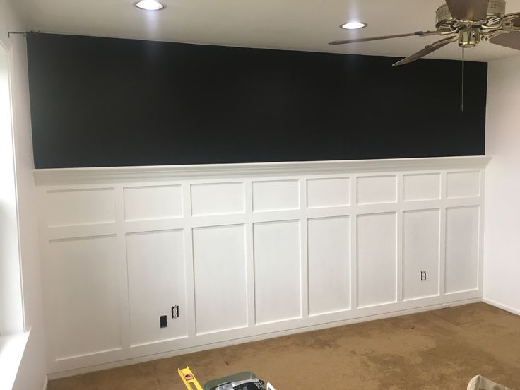 an empty room with white paneling and a ceiling fan