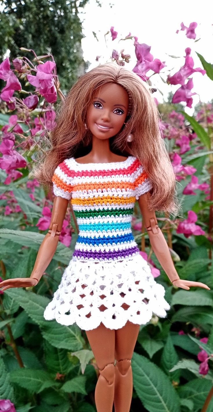 a doll is standing in the middle of some purple flowers and wearing a colorful crochet dress