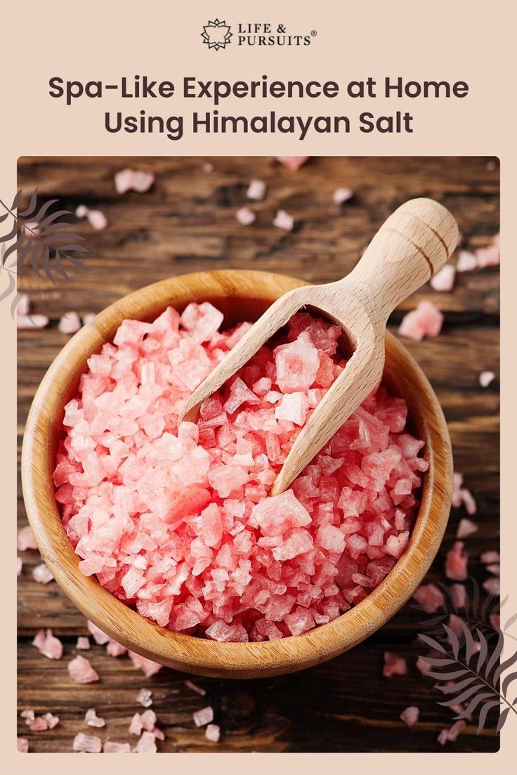 a wooden bowl filled with pink sugar on top of a wooden table next to a spoon