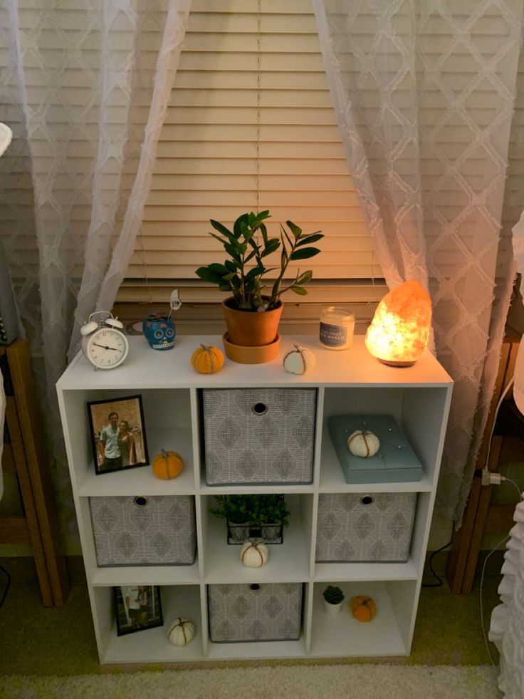 a white shelf with some plants on top of it next to a lamp and window