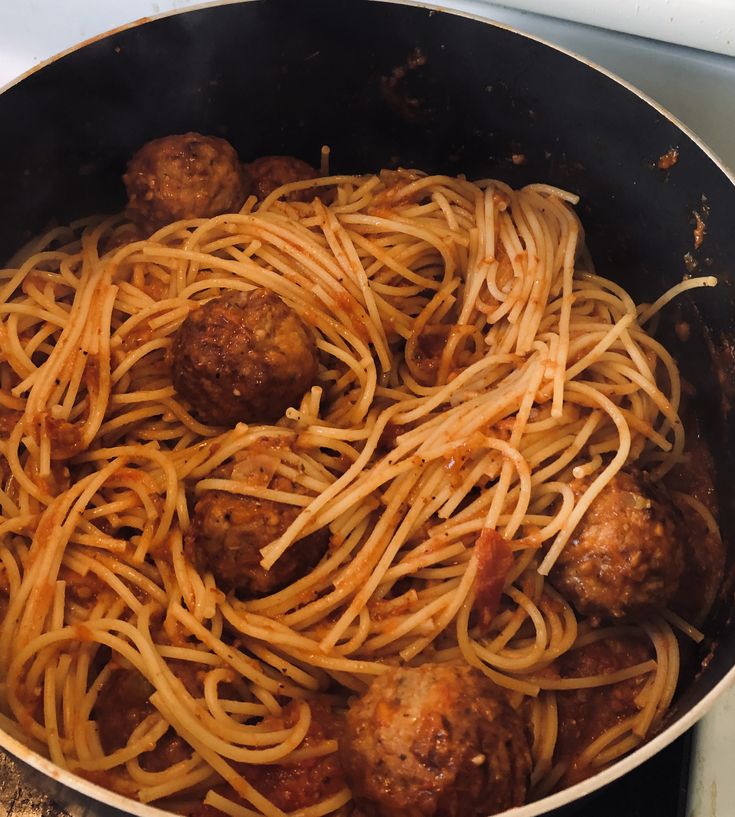 spaghetti and meatballs are being cooked in a pan