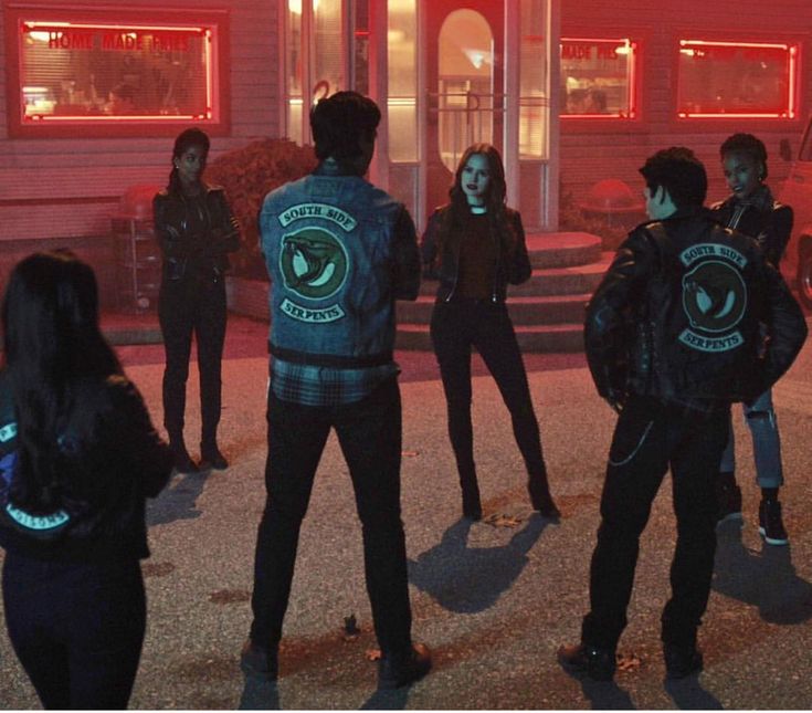 group of people standing in front of a building at night with neon lights on their backs