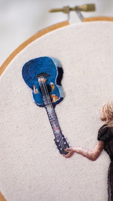 a woman holding a blue guitar in front of a wall hanging on a wooden frame