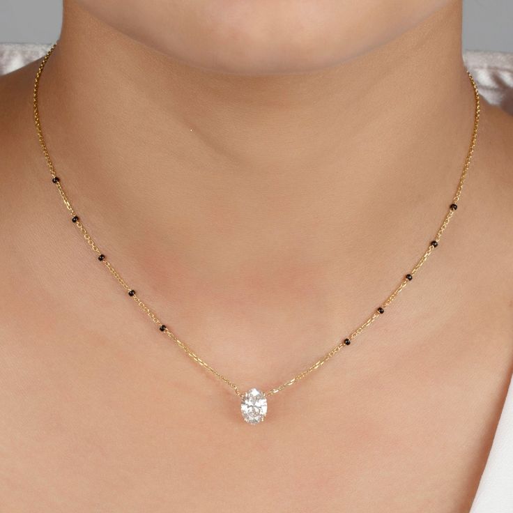 Discover the Deepika Mangalsutra, where timeless tradition meets modern sophistication. This elegant necklace features a vertically set brilliant oval certified lab-grown diamond in a fixed pendant, with options ranging in diamond size and grade. Crafted from luxurious 18k gold—available in yellow, white, or rose—it is accented with five evenly spaced black beads on each side of the chain and a diamond ranging in size and grade. The Deepika Mangalsutra transcends mere adornment; it's an embodime Deepika Mangalsutra, Luxury Elegant Black Mangalsutra, Black Beads Models, Black Beads Diamond Pendant, Elegant Solitaire Necklace With Oval Pendant For Formal Occasions, Elegant Oval Pendant Solitaire Necklace For Formal Occasions, Elegant Formal Solitaire Necklace With Oval Pendant, Elegant Jewelry With Single Cut Diamonds In Oval Pendant, Elegant Oval Pendant Jewelry With Single Cut Diamonds