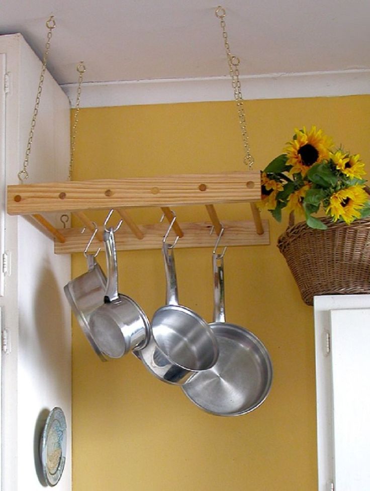 pots and pans hanging from hooks in a kitchen with sunflowers on the wall