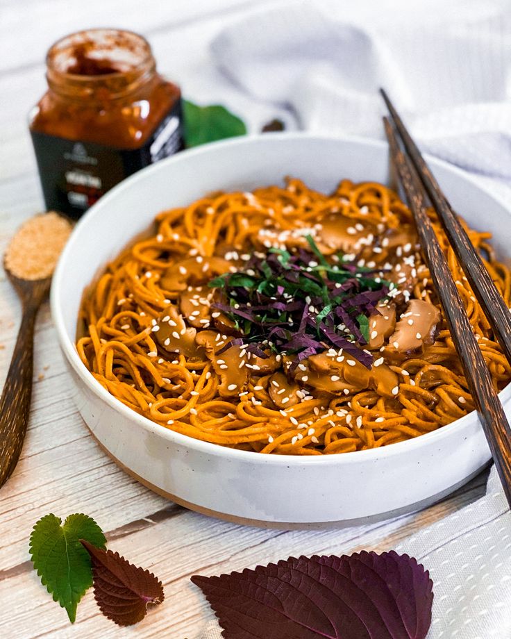 a bowl of noodles with chopsticks next to it on a white tablecloth