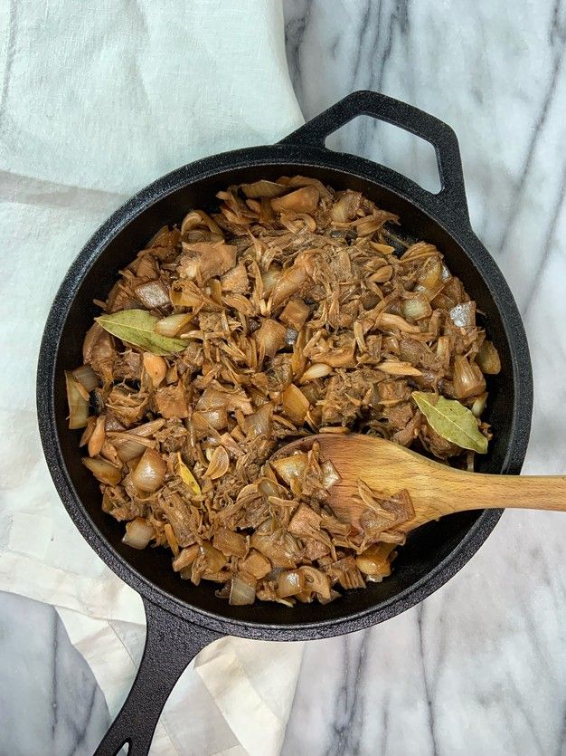 a skillet filled with meat and onions on top of a marble countertop next to a wooden spoon