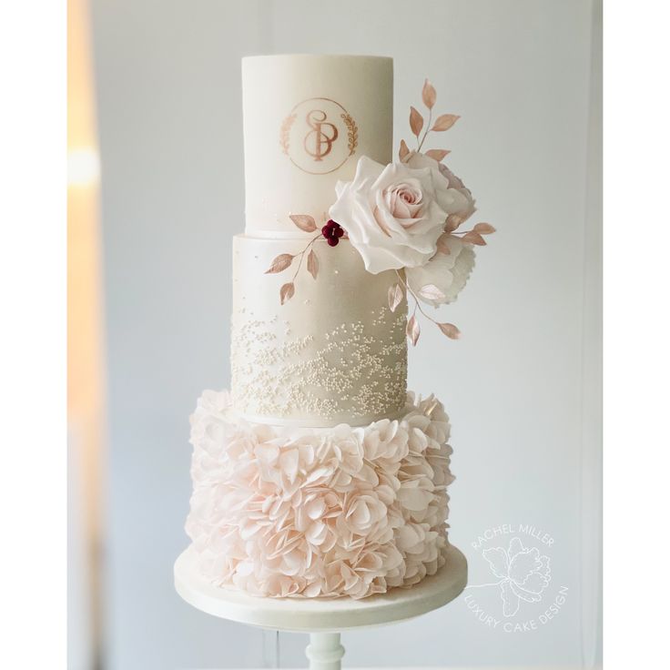 a three tiered white wedding cake with pink flowers and monogrammed initials on top