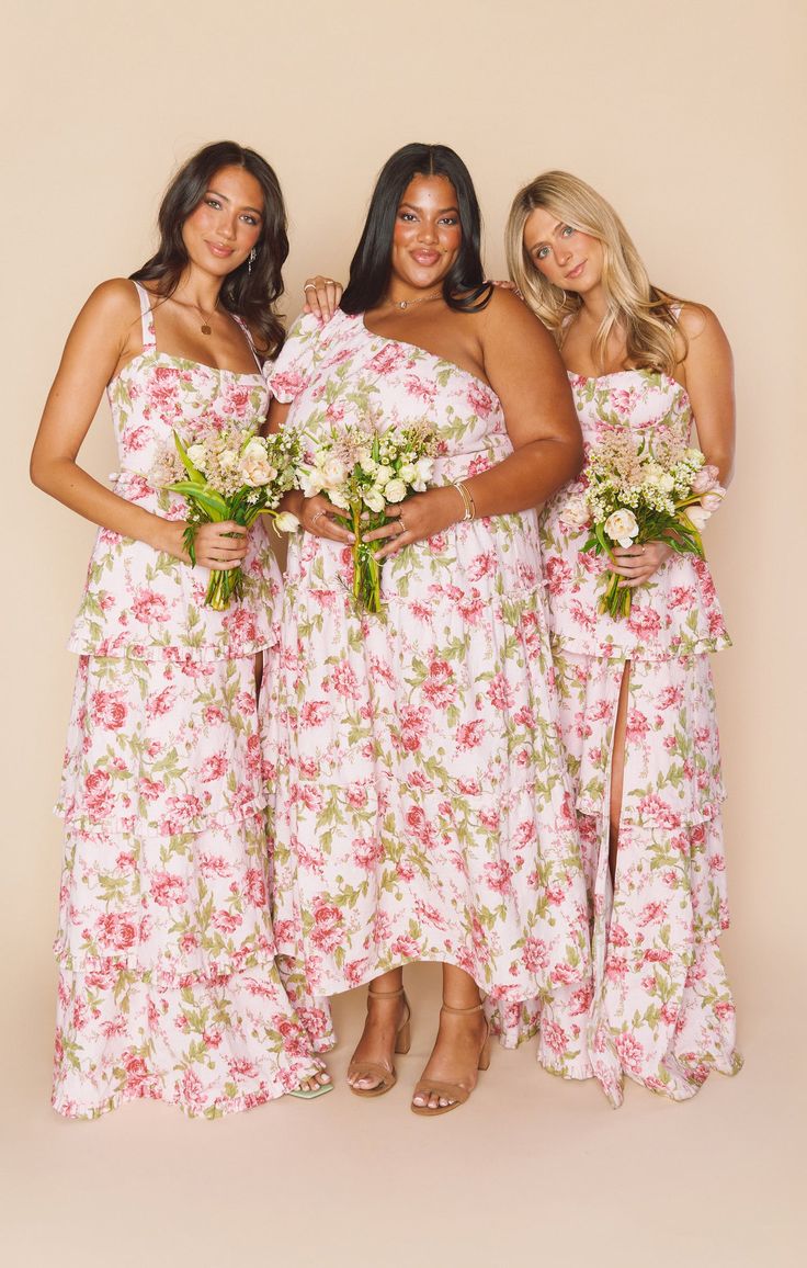 three women in dresses standing next to each other with flowers on the bottom and one holding a bouquet