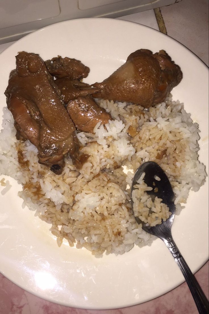 a white plate topped with rice and meat next to a spoon on top of a table